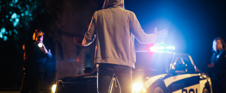 A man stands in front of a police car, illuminated by the night lights, creating a tense atmosphere