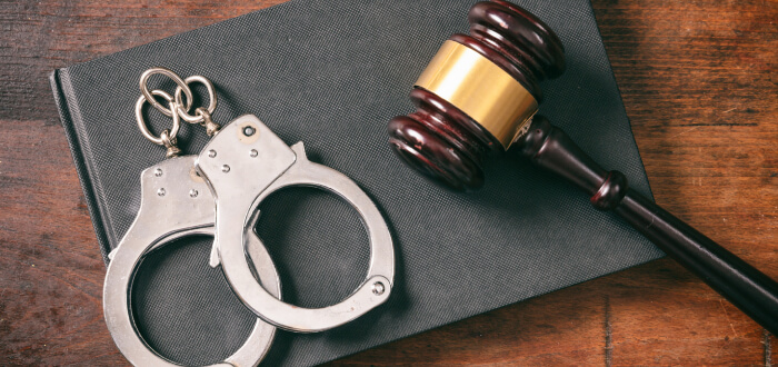 Handcuffs and a gavel resting on a wooden table, symbolizing law enforcement and the judicial system