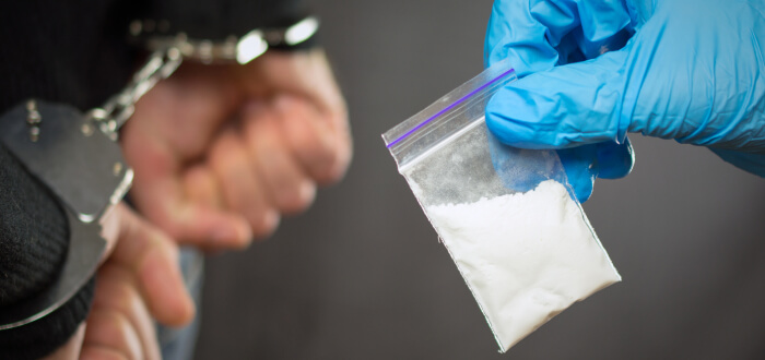 A police officer holds a person's hand containing illegal drugs, emphasizing law enforcement's role in combating drug-related issues