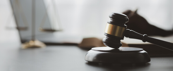 A judge's gavel rests on a wooden desk alongside a laptop and several books, symbolizing legal proceedings and research