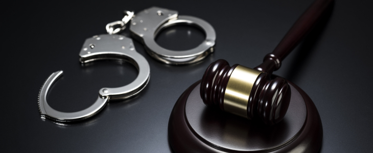 Handcuffs and a gavel placed on a black background, symbolizing law enforcement and the judicial system