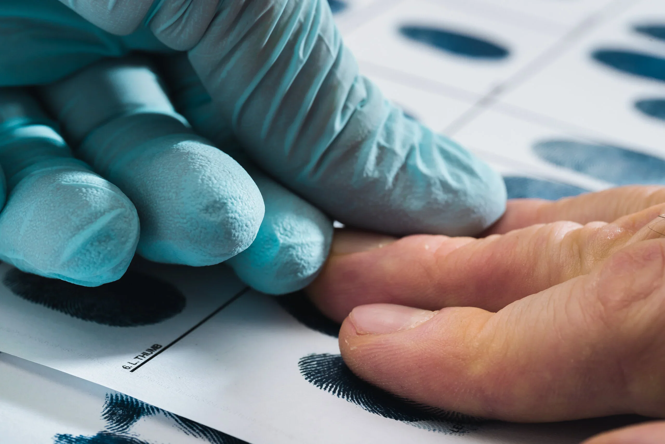 A person wearing blue gloves points at a piece of paper, indicating a specific detail or instruction