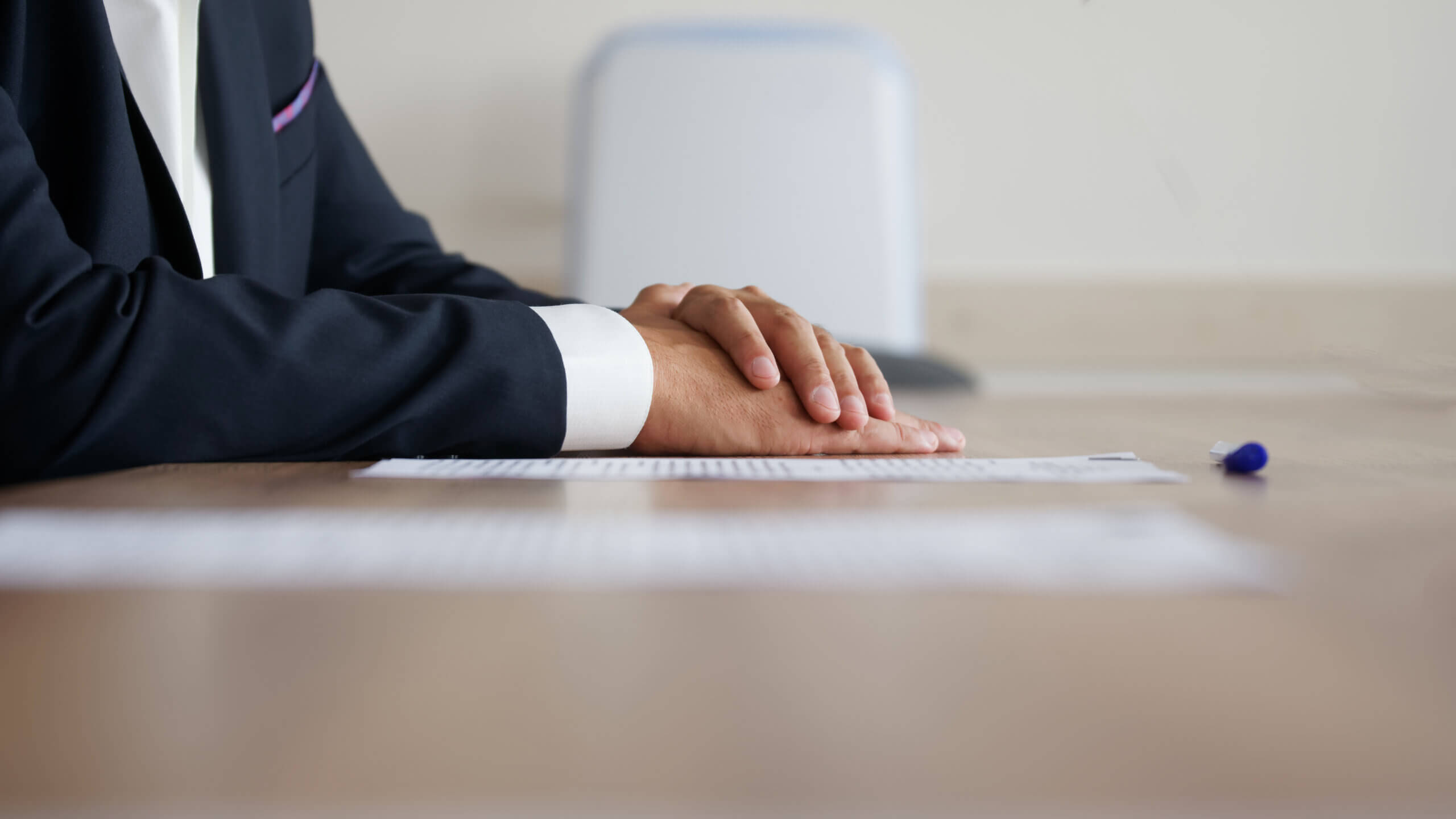 A man in a suit sits at a desk with his hands folded, exuding professionalism and contemplation