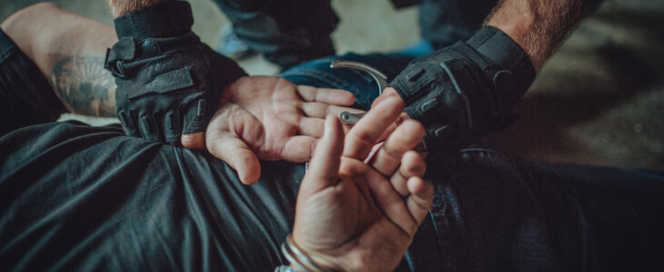 A man is being handcuffed by another man, indicating a law enforcement or security situation