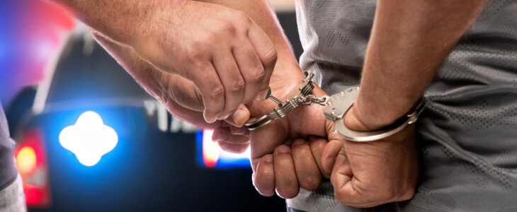 Two police officers display handcuffs in front of a police car, symbolizing law enforcement and public safety