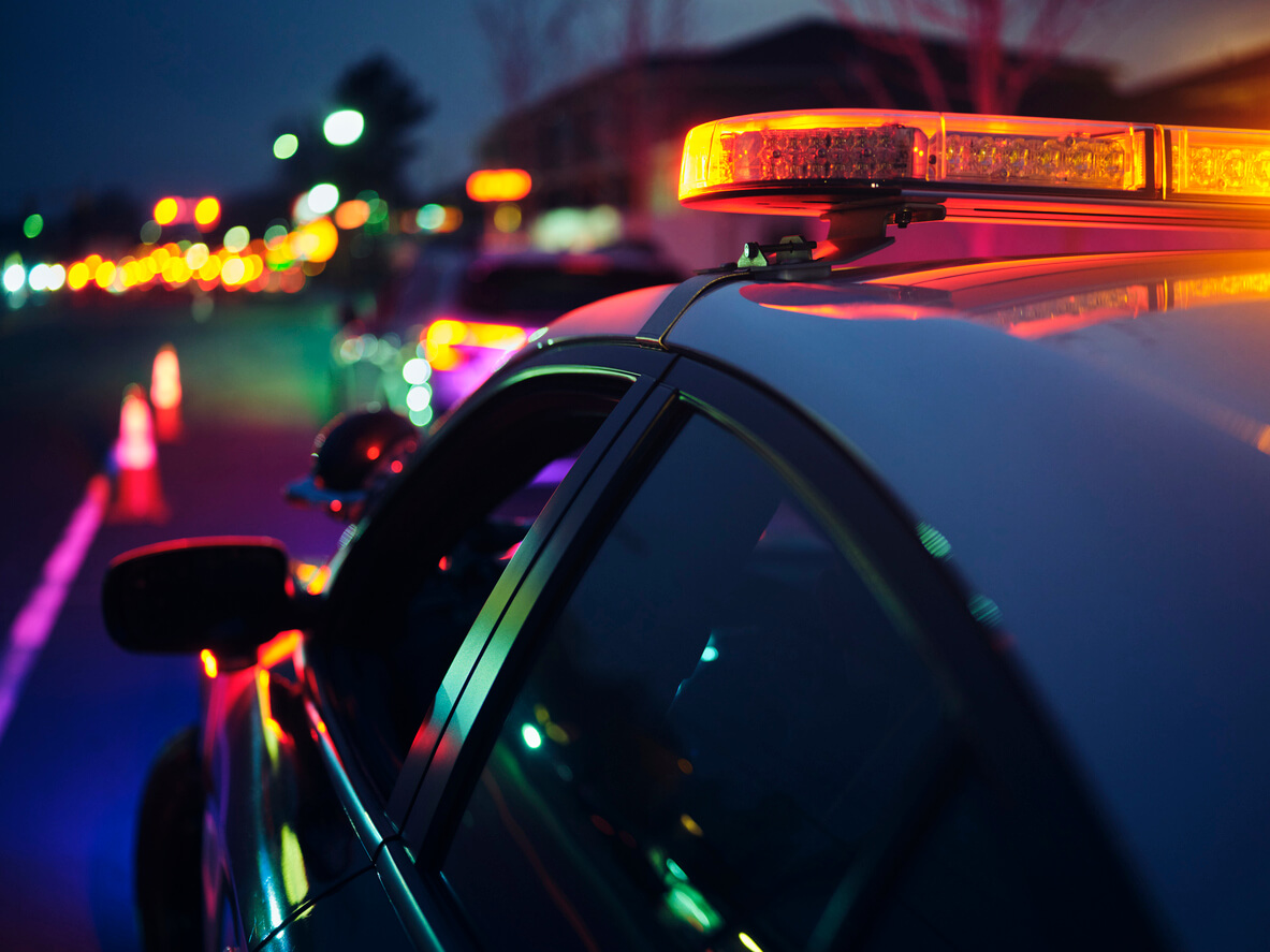 A police car with its flashing lights activated, parked on the street, signaling an emergency response situation